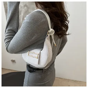 Close-up of white croc-embossed shoulder bag with a gold buckle and knotted strap details