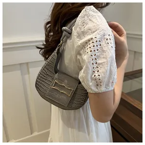 Detail of grey crocodile embossed crescent bag with gold buckle and knotted shoulder strap