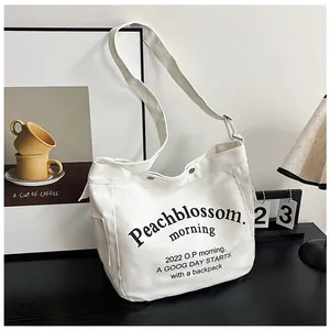 Détail du sac cabas en toile blanche avec imprimé lettres, poche latérale et bandoulière