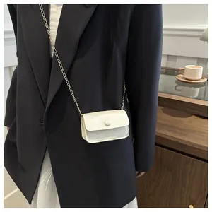 Detail shot of a mini cream white crossbody bag with pearl accent and gold chain strap