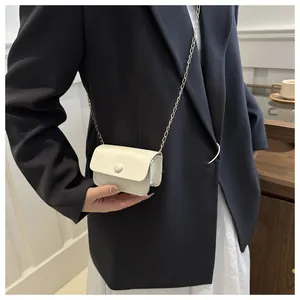 Close-up of a white leather mini bag with a fine gold chain strap worn by a model