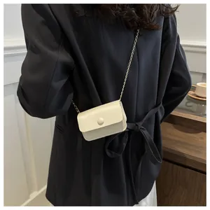 Detail of a mini cream white crossbody chain bag worn over a dark navy blazer