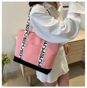 Détail d'un sac cabas en toile rose avec garniture noire et bretelles à motif lettres