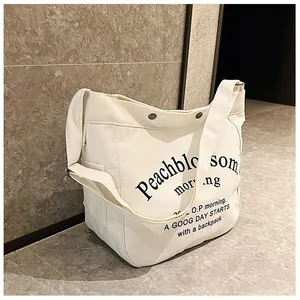 Détail du sac fourre-tout en toile crème avec typographie noire et rivets métalliques