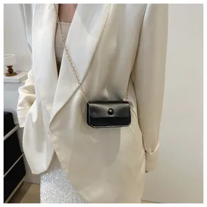 Mini black crossbody bag with gold chain strap worn over white blazer and sequin skirt