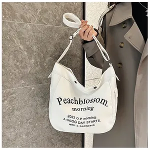 Détail du sac fourre-tout en toile blanche avec lettrage noir et bandoulière sur un trench gris