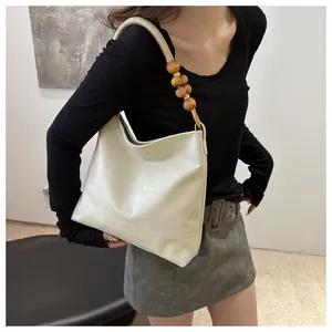Detail of hobo bag featuring soft cream faux leather and decorative wooden beads strap