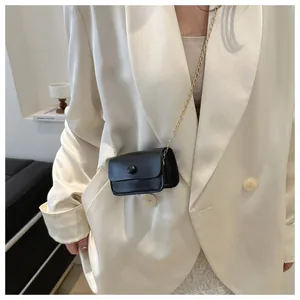 Close-up of black leather mini crossbody bag with gold chain strap on a model outfit