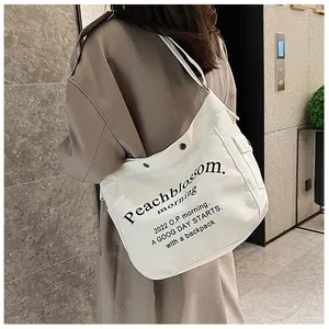 Détail du sac fourre-tout en toile blanche avec lettrage noir sur un trench marron