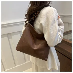 Brown leather tote bag featuring patchwork detail and unique wooden bead strap decorations