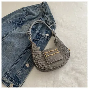 Detail of grey crocodile embossed texture with golden rectangular clasp on underarm bag