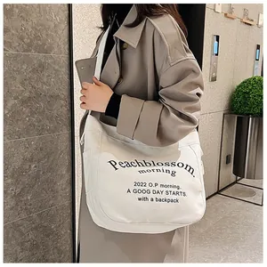 Femme en trench kaki portant un grand cabas en toile blanche avec imprimé lettrage
