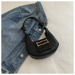 Detail of black faux leather crescent bag with crocodile texture and gold hardware