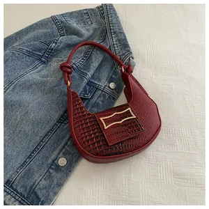 Detail of burgundy leather crescent bag with crocodile texture and golden metal buckle