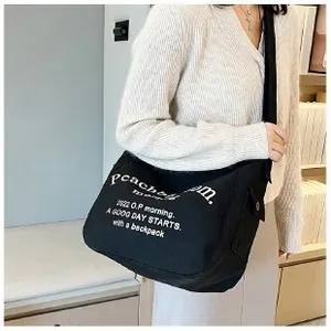 Détail du cabas en toile noire avec lettrage artistique blanc et poche latérale à pression