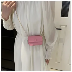 Close-up of a mini pink crossbody bag with a round buckle and gold chain strap
