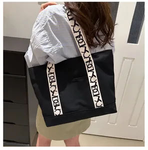 Détail d'un grand sac cabas en toile noire avec bandoulière à motifs et poche extérieure