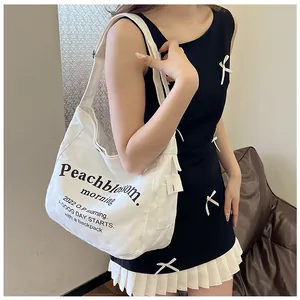 Détail du sac fourre-tout en toile blanche avec lettrage noir et large bandoulière