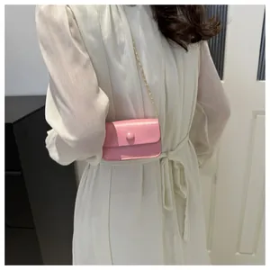 Detailed view of mini pink leather crossbody bag with gold chain strap on white dress
