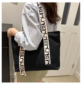 Détail d'une bandoulière crème avec lettrage noir sur un grand sac cabas en toile noire