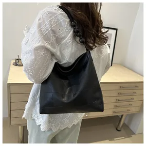 Detail of black woven tote bag with beaded shoulder strap in a minimalist interior setting
