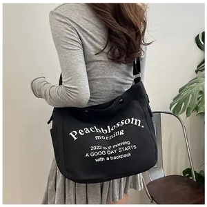 Détail d'un sac cabas en toile noire avec lettrage blanc et bandoulière réglable