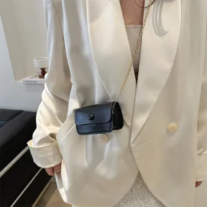 Chic mini black leather crossbody bag with gold chain strap shown on model in beige blazer