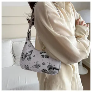 Artistic underarm bag with butterfly print shown on shoulder of model in soft light