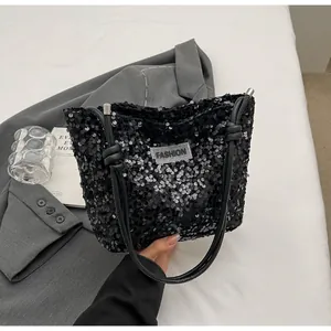Close-up of black sequined tote bag with knotted handles and fashion label on front