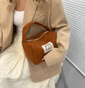 Dettaglio della borsa in velluto a coste marrone con toppa a orso e blazer beige