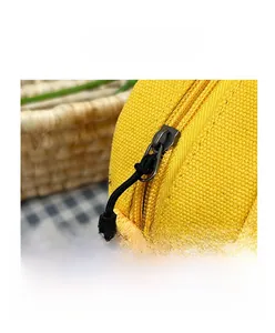 Detail of yellow canvas bag featuring a black metal zipper and woven pull rope closure