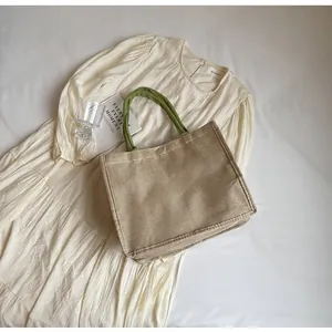 Gros plan d'un sac cabas tissé crème avec poignées vertes sur une robe plissée