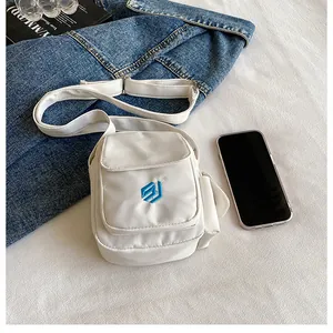 Close-up of white mini nylon crossbody bag with blue embroidery and front flap pocket