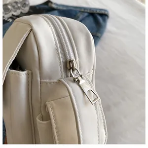 Detailed view of the side zipper, flap pocket, and stitching on a white outdoor crossbody bag