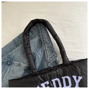 Close-up of a black quilted tote bag featuring white TEDDY text and puffy padded handles