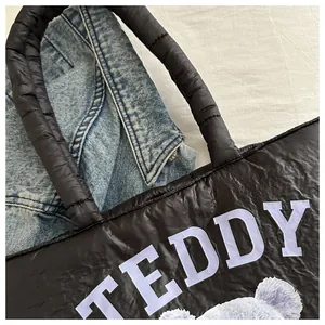 Detailed macro view of black quilted tote bag with purple teddy bear and lettering print