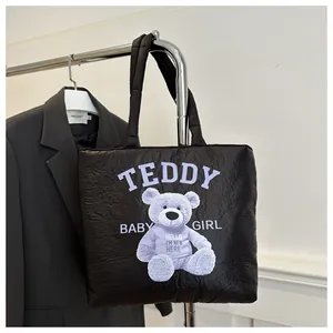 Detail of black quilted tote bag featuring a purple teddy bear print and soft handles