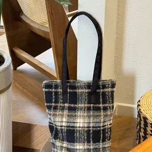 Gros plan d'un grand sac cabas en tweed à carreaux avec anses noires dans un salon