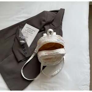 Detail of white quilted backpack with colorful embroidery on bed with lifestyle props