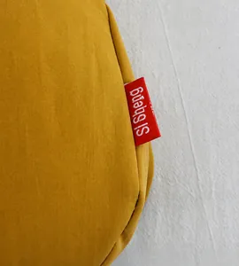 Detail view of ginger yellow canvas fabric with a woven red brand logo on the crossbody bag