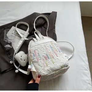 Close-up of white mini backpack with colorful wave embroidery and cloud plush charm