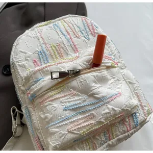 Detail of white mini backpack fabric with wavy colorful embroidery and diamond texture