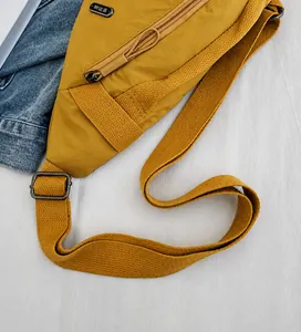 Detail of adjustable woven strap and metal buckle on yellow nylon crossbody chest bag