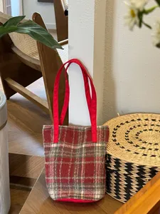 Détail du sac cabas en laine à carreaux rouges avec fines anses dans un décor intérieur