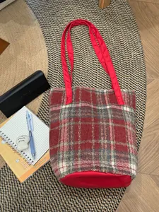 Détail du sac cabas en laine à carreaux rouges avec longues anses sur tapis et bois