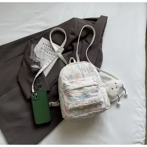 Close-up of a white quilted mini backpack with colorful embroidery and a cloud plush charm