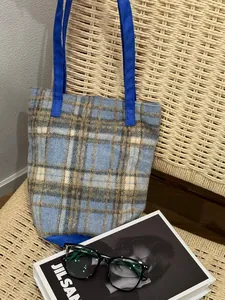 Détail d'un cabas en laine à carreaux avec sangle bleu roi et texture tissée sur chaise