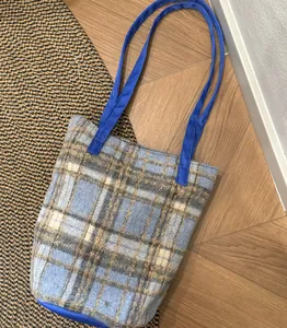 Vue détaillée du grand sac à bandoulière en laine à carreaux bleus sur un sol en bois