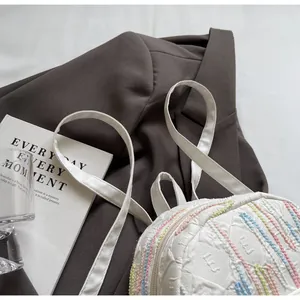 Detail of white textured mini backpack with pastel wavy lines and embossed letter E