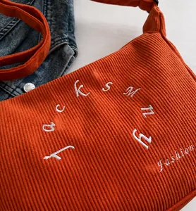 Detail of orange corduroy tote bag showing embroidered lettering and vertical texture